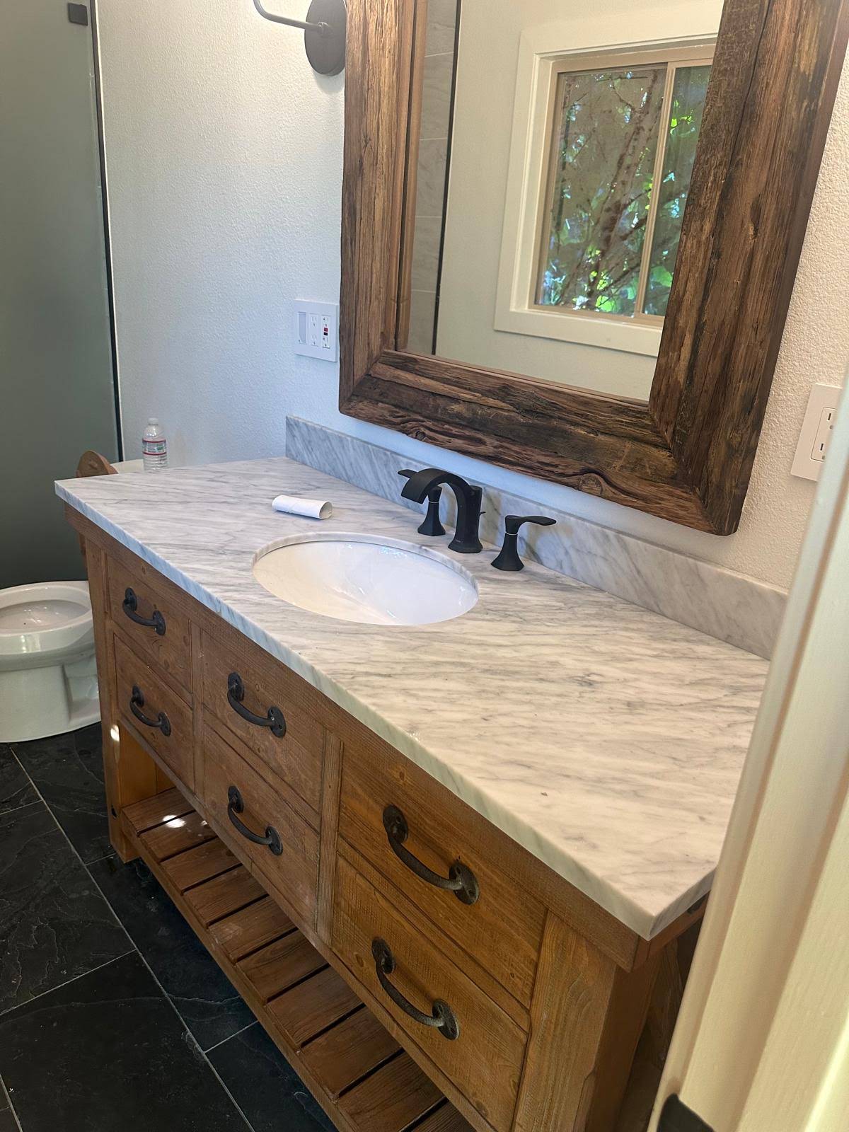 Bathroom vanity with stone top, dark fixtures, and wood-framed mirror
