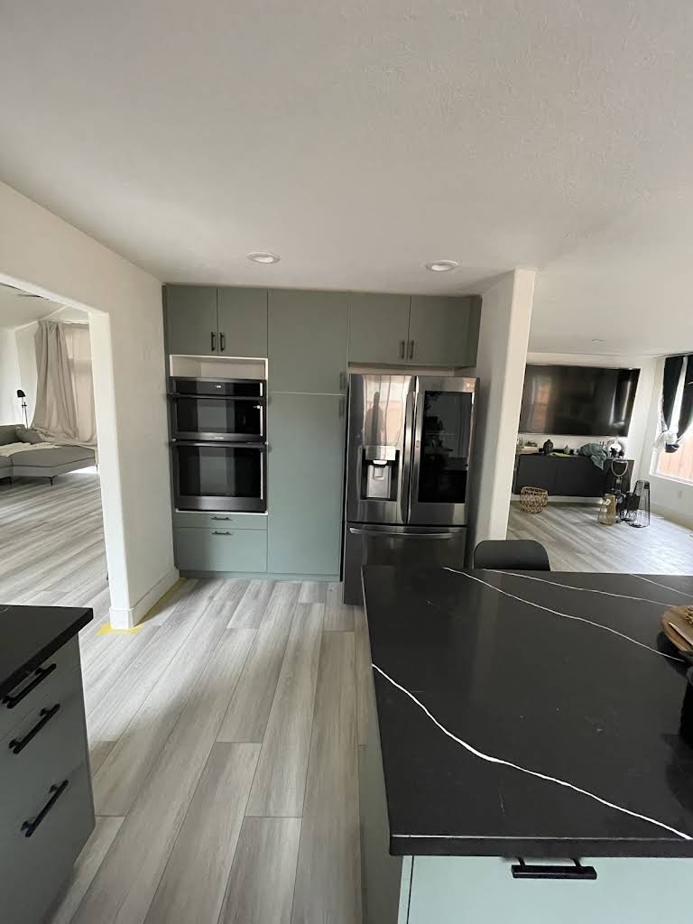 Finished kitchen remodel with green cabinets and a dark island