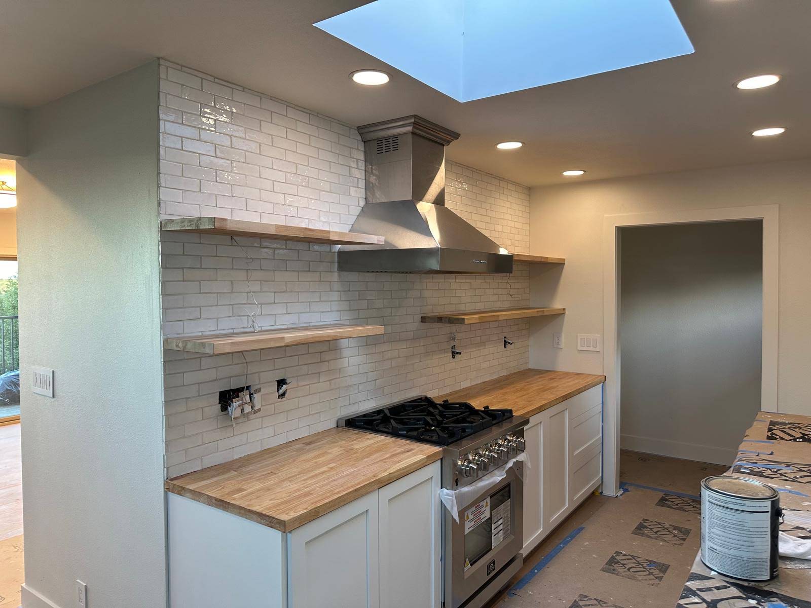 Kitchen renovation with white cabinets, wood counters, range hood, and skylight